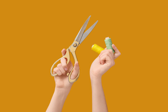 Sewing and crafting hobby, hands holding scissors and thread spools, DIY fashion and textile art on orange background