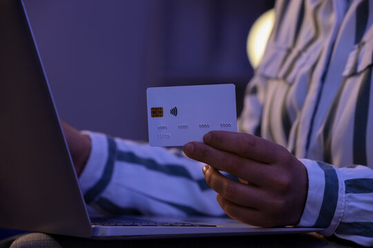 Young woman with credit card using laptop for online shopping on sofa in evening at home, closeup