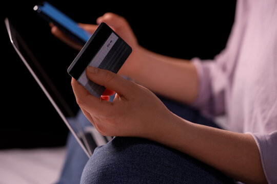 Young woman with credit card and mobile phone using laptop for online shopping on bed in evening at home, closeup