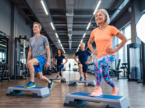 Diverse group of active seniors and mature adults performing step aerobics lunges in a bright modern gym.