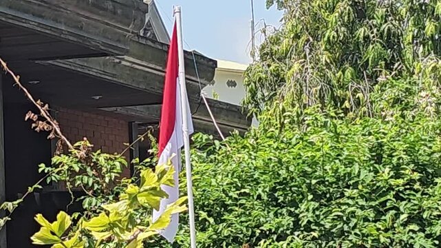 old brick wall,Red and white flag waves gently in a lush green garden. Bright sunlight illuminates vibrant leaves Flagpole stands tall beside thick foliage Indonesian Independence day
