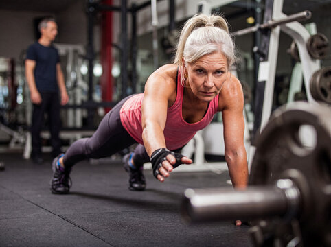 Determined senior woman performing a challenging one-arm push-up exercise in a modern gym.