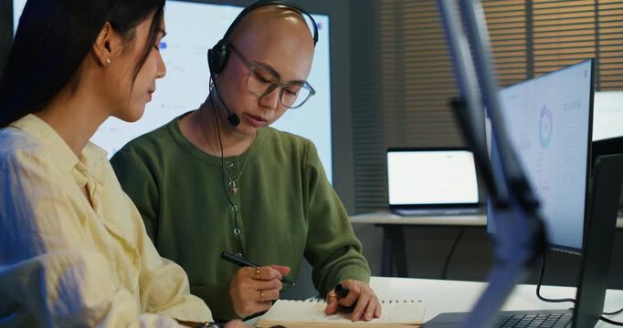 Colleagues working late on digital customer service, using headsets and computers to provide online support, teamwork, and professional expertise in a call center environment.