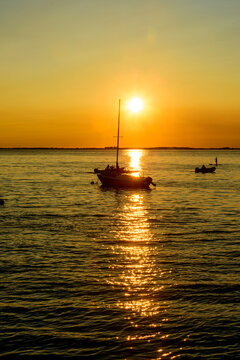 Golden Sunset Over Water with Silhouetted Sailboat and Small Watercraft