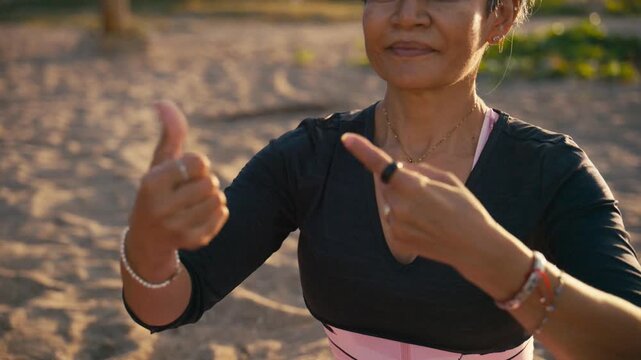 Senior woman practicing gentle and flowing hand gestures of tai chi outdoors on a sandy surface