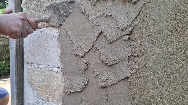 Construction Worker Applying Concrete Mortar to Brick Wall Using Trowel for Plastering and Building Renovation Work
