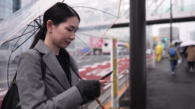 雨の街でスマートフォンを見る女性