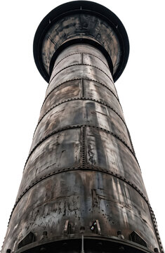 Low angle upward shot of a tall cylindrical industrial metal chimney stack showing weathered surface plates held together by rivets and bolts under bright daytime lighting conditions