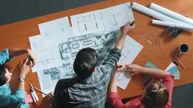 Group of people looking at blueprint while brainstorming idea. Top view of engineer team looking and planning house construction by using blueprint. Engineer hold paper while point at plan. Symposium.