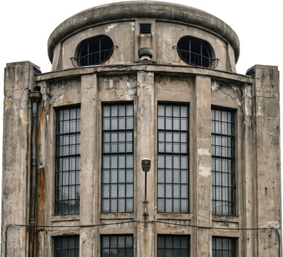 Architectural facade of an old industrial concrete building featuring tall gridded windows and a rounded top section with weathered textured surfaces and distressed exterior details
