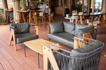 Fototapeta premium Empty cozy tropical cafe interior featuring a white table, woven rattan chairs with cushions, wooden flooring, and large wooden pillars against a white wall near glass folding doors.