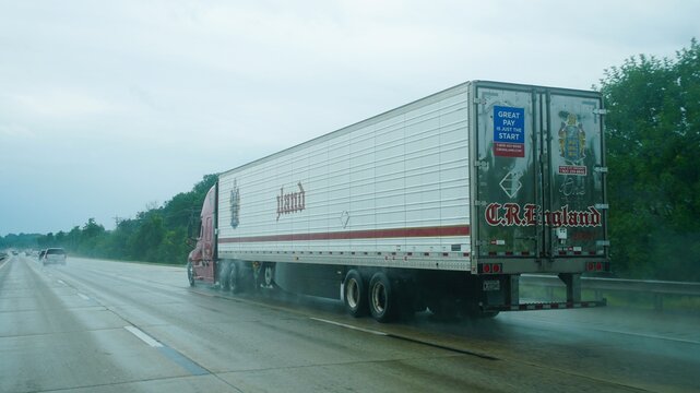 Wilmington, Delaware, U.S.A - August 16, 2026 - C.R. England semi-truck drives on a wet highway, displaying company branding and recruitment signage on its trailer.