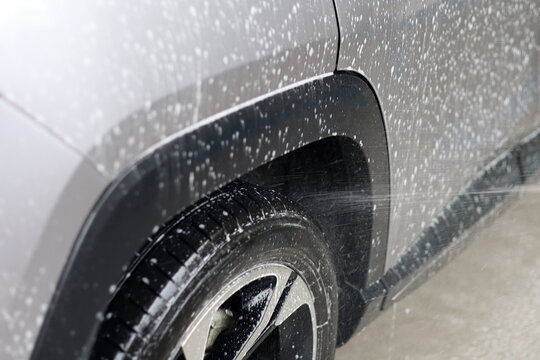 Washing soapy silver car with high pressure water spray.