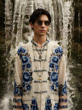 Fashionable portrait of a stylish man standing in front of a misty natural waterfall