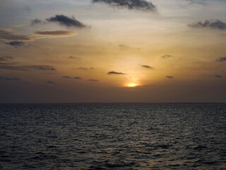 Fototapeta premium The setting sun dips toward the horizon behind scattered clouds, casting a warm golden glow across the calm Atlantic Ocean off Gorée Island, Senegal