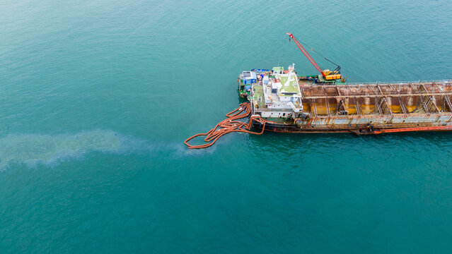 Oil spill Industrial response ship deploying an orange containment boom to control and clean up a marine pollution spill in the open ocean, protecting the sea ecosystem from hazardous chemical waste.