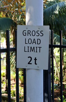 A white rectangular sign mounted on a post stating "GROSS LOAD LIMIT 2t" against a black metal fence background