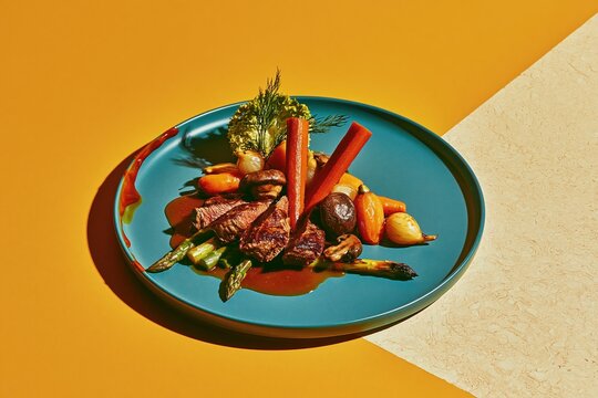 Sliced beef steak with glossy pan jus and roasted vegetables on a teal plate, featuring rich golden tones for restaurant menus and dining campaigns