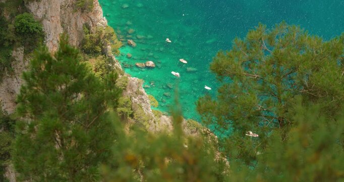Turquoise coastal water with small boats below steep rocky cliffs in Capri Italy