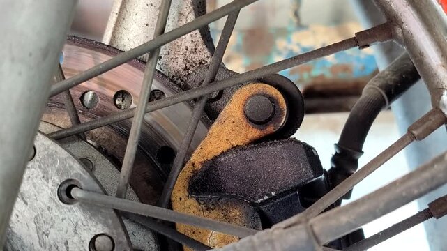 Dirty worn motorcycle disc brake close up showing brake caliper, old rotor, and brake pad needing repair and maintenance