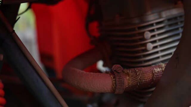 Vintage motorcycle engine with rusted exhaust pipe, weathered metal cooling fin detail, armored warrior with curved sword beside red garment, dramatic low light and rugged mechanical texture