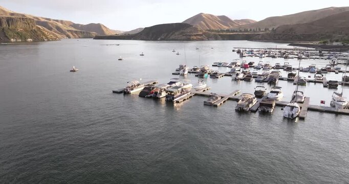 Marina at golden hour, boats moored, calm water, scenic hills