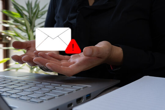 Hands hold email icon with warning symbol. Person sits at laptop desk. Image shows message alert or email problem. Suitable for tech support, cybersecurity, or communication issues