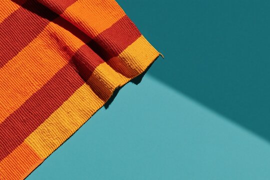 Handwoven kente cloth with vibrant orange and gold patterns on a teal surface, featuring a ribbed texture for cultural heritage and textile design