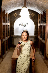 Naklejka premium Elegant woman enjoys fine wine in a cozy cellar during a tranquil evening