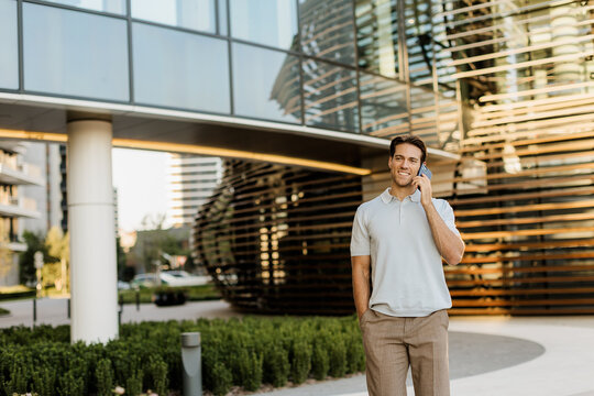 Smiling man on the phone in modern urban setting during sunny day