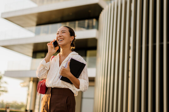 Cheerful woman talking on the phone outside a modern office building