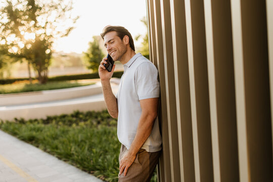 Man on a call, leaning against modern architecture at dusk