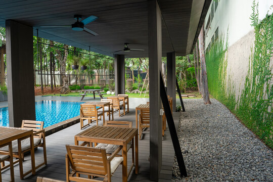 Modern outdoor poolside cafe patio with wooden dining sets and climbing ivy creeping fig wall.