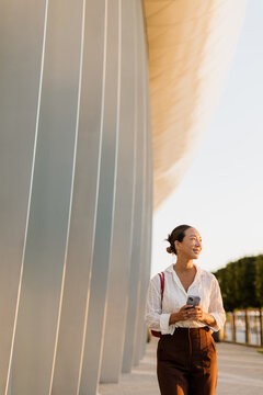 Korean woman enjoys a sunny moment near a modern architectural masterpiece