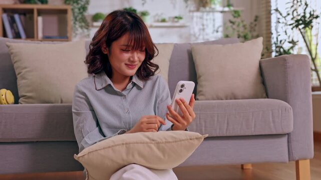 Smiling woman using smartphone on sofa in cozy living room with pillow casual indoor home scene sitting texting near cushion plant soft daylight