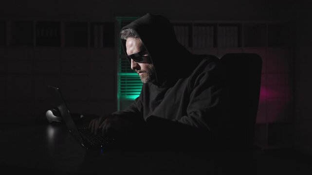 Cybercrime hackers risks online privacy. Anonymous hacker typing code in dark office. Hooded hacker in cyber crime activity. Office hackers. Cyberattack, digital breaking and malware concept.