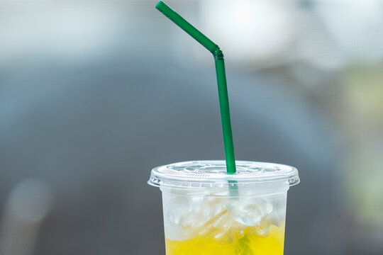 Iced yellow beverage in a plastic cup with a green flexible straw.A refreshing close-up shot of a cold