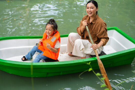 mother and preschool child girl in a green paddle boat on a scenic pond.
