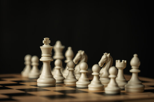 white chess pieces on a wooden board, on black background