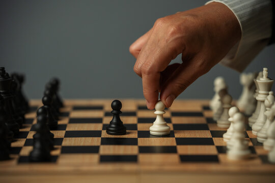 business hand moving a white pawn on wooden chessboard, strategy