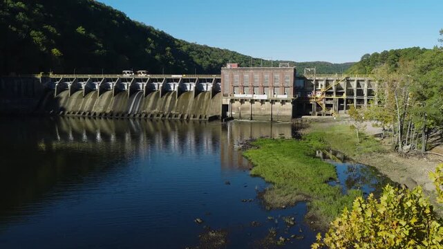Wide aerial ascend past trees of Remmel Dam with calm reservoir and shoreline, drone backdrop, Ouachita River Jones Mill Arkansas USA