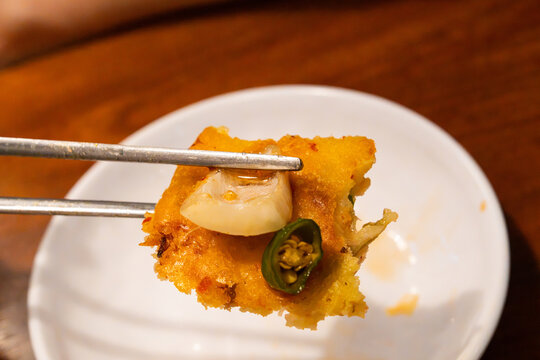 Metal Chopsticks Holding Crispy Bindaetteok Bite with Pickled Onion and Chili