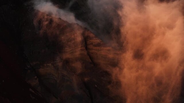 Ethereal clouds swirl across Mount Rinjani crater wall in golden morning light, aerial overview of textured banded slopes