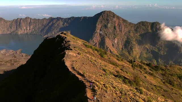 Hikers follow Mount Rinjani ridge above the caldera in crisp morning light, aerial tracking with dark shadow side of slopes, Indonesia adventures