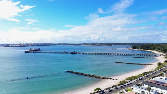 Kurnell shoreline with long pier and calm turquoise waters, aerial establishing dolly over suburb homes along white sands, Kurnell NSW Australia