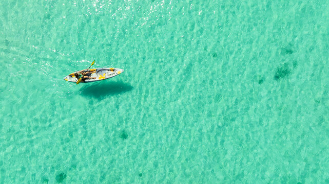 Aerial view of a woman and a young man kayaking on clear blue waters at Andaman Island. She does water sports activities.	

