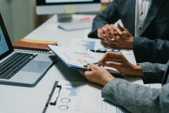 Business professionals reviewing charts and graphs on documents, discussing market strategy and financial reports in an office setting