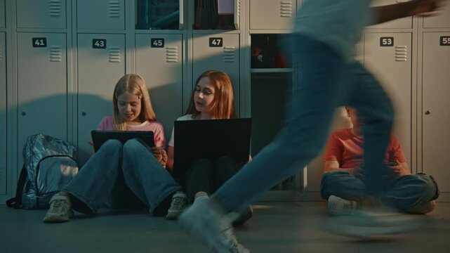 Three Classmates Sitting Casually Against Row of Lockers Bathed in Cinematic Sunlight. Girls Sharing Screen Time on Laptop, Boy Completely Focused on Mobile Phone. Modern Childhood, Digital Natives.