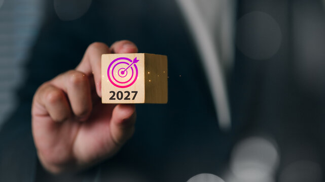 A professional businessman presenting a wooden cube with a target symbol and the year 2027, symbolizing future goals, planning, and strategic success.