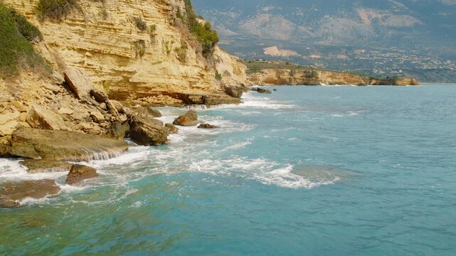 Turquoise sea waves hitting rocky shoreline beneath steep cliffs in Kefalonia